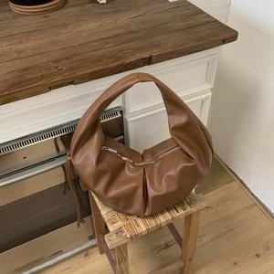 Close-up of brown pleated shoulder bag with silver zipper on a wooden stool