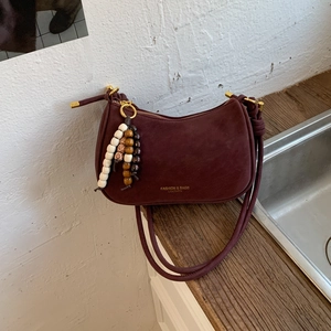 Detail of burgundy suede half-moon crossbody bag with vintage gold hardware and bead charm