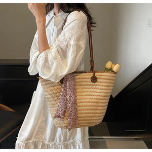 Detail of woven straw tote bag featuring brown leather straps and vintage paisley scarf
