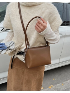Close-up of warm brown faux leather shoulder bag with peanut charm and metal chain detail