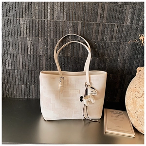 Detail of beige tote bag with geometric texture and leather horse charm on a desk