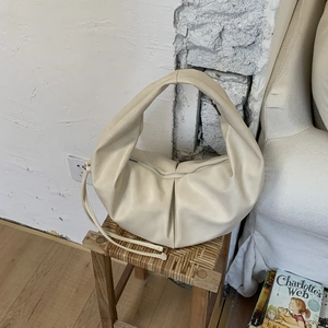 Creamy beige crescent shoulder bag with soft pleats displayed on a woven stool