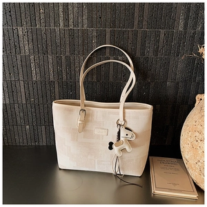Detail of a beige tote bag featuring a leather patch and a horse-shaped hanging charm