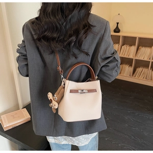 Detailed view of beige lychee leather bucket bag with brown handles and cute plush charm