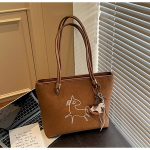 Close-up of brown suede shoulder bag with pony pattern and wooden rocking horse charm