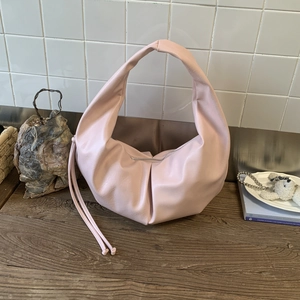 Detail view of pink half-moon hobo bag with pleated bottom and long drawstring on wood