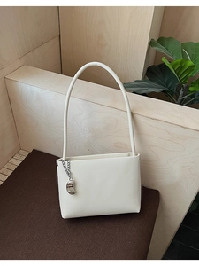 Detail of minimalist white underarm bag with a silver metallic pendant charm