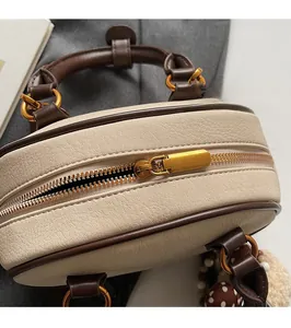 Detailed top view of beige barrel bag featuring smooth gold zipper and brown piping