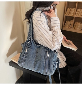 Detailed view of blue washed denim tote bag with silver zippers worn by a model