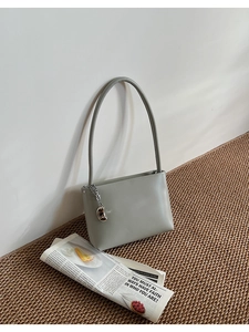 Detail of gray leather shoulder bag featuring a silver metal bean pendant and clean texture