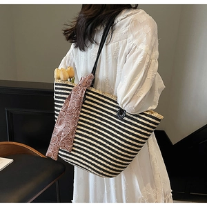 Detail of striped woven straw tote bag with black and white fringes and red silk scarf