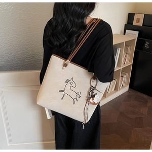 Detail view of a beige tote bag with brown leather trim and stylish horse totem print