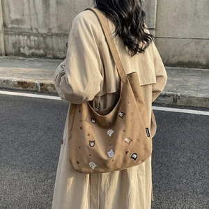Brown corduroy tote bag with cat embroidery and shoulder strap worn by model in street view