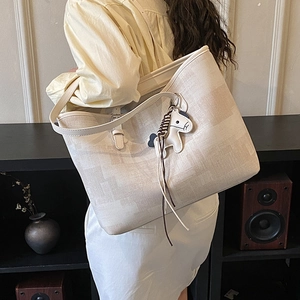 Detail of large beige woven tote bag with horse pendant on shoulder of a model