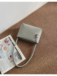 Detailed macro view of minimalist grey leather handbag with silver cashew pendant and chain
