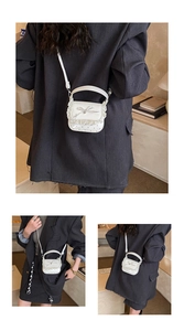 Detail of white mini lace crossbody bag with silver bow and heart cut-outs on a grey blazer