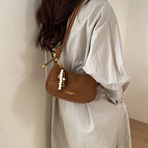 Detail of a brown suede hobo bag featuring a wooden bead tassel and gold logo lettering