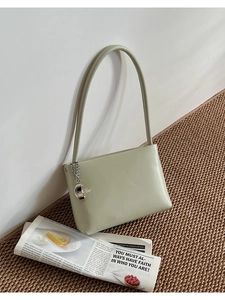 Detail of sage green matte leather shoulder bag with chic silver bean-shaped metal pendant