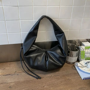 Detailed view of black pleated PU leather dumpling bag with soft texture and side tassels