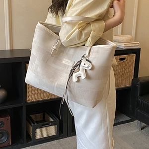 Detailed close-up of a large canvas tote bag with leather trim and horse charm