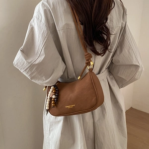 Detail view of brown leather half-moon bag with decorative beads and knotted shoulder strap