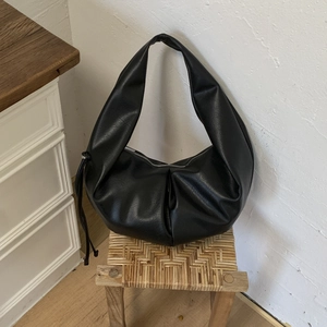 Detail of black faux leather hobo bag showing textured pleats and crescent design on a stool