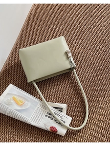 Detail of light green rectangular shoulder bag with silver chain on woven mat