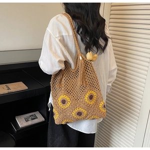 Detail of woven straw tote bag with yellow sunflower patterns and bohemian tassels