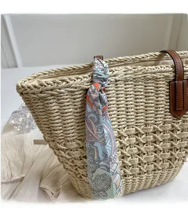 Detail of woven straw tote bag featuring brown leather handles and a floral silk scarf tie