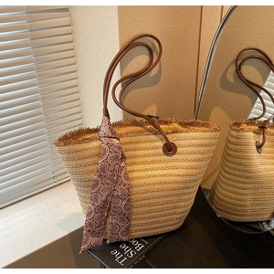 Close-up of woven straw tote bag with fringe edge, leather handles and silk scarf detail