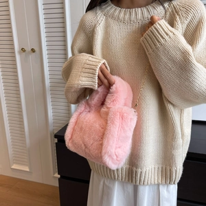 Petit sac seau rose en fausse fourrure avec chaîne dorée sur un pull beige d'hiver