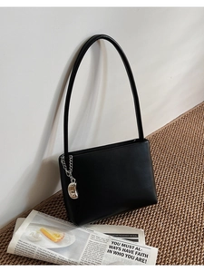 Detail of minimalist black matte handbag with silver bean charm and slender strap