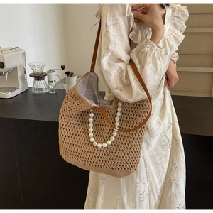 Detail of woven straw tote bag with pearl handle and brown leather strap on model