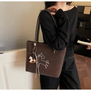 Detailed view of dark brown tote bag featuring horse embroidery and wooden horse pendant