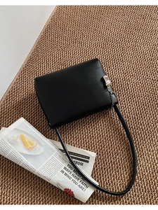 Detail of black leather shoulder bag with silver car-shaped charm on woven texture