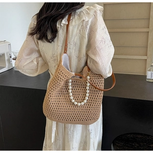 Detail of hand-woven straw tote bag featuring white faux pearl handles and brown leather strap