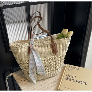 Detail of woven straw tote bag with brown leather handles and decorative floral scarf