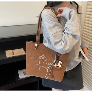Close-up of brown suede tote bag with minimalist horse pattern and horse charm