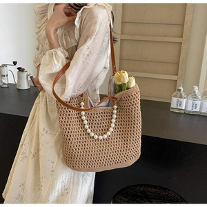 Detail of hand-woven straw tote with pearl chain strap and brown leather handle