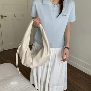 Detail view of cream-colored leather crescent bag with side drawstring details on a model