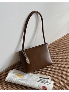 Detail of dark brown leather shoulder bag with silver decorative chain and metal pendant