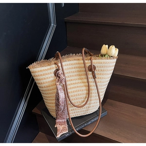 Detail of striped straw tote bag featuring tassel fringe and paisley silk scarf handle
