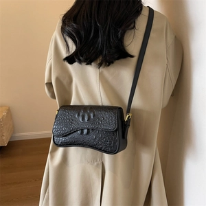 Dettaglio della borsa a tracolla nera effetto coccodrillo su un trench coat beige