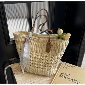 Detail of woven straw tote bag with brown leather handles and decorative silk scarf