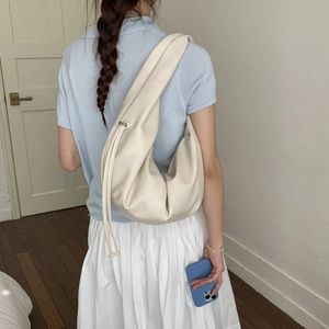 Creamy white hobo bag with drawstring details shown on shoulder in a minimalist room