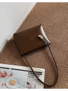 Close-up of dark brown matte leather handbag with silver oval metal buckle on woven mat