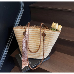 Detail of striped straw tote bag with brown leather handles and a paisley silk scarf décor