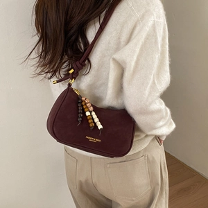 Detail view of burgundy suede dumpling bag with decorative beads and golden fashion logo