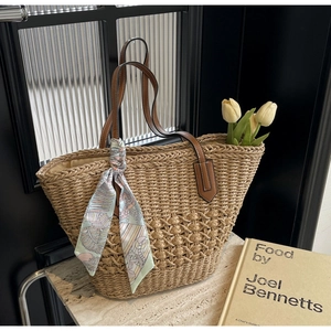 Detail of hand-woven straw tote bag with leather straps and decorative floral silk scarf