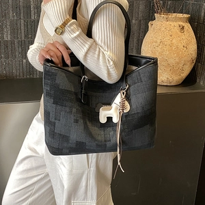 Detail of commuter tote bag featuring pixel texture and white horse charm accessory